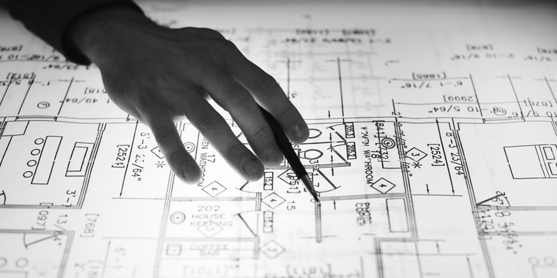 Hand of architect holding pen pointing to architectural blueprint plans